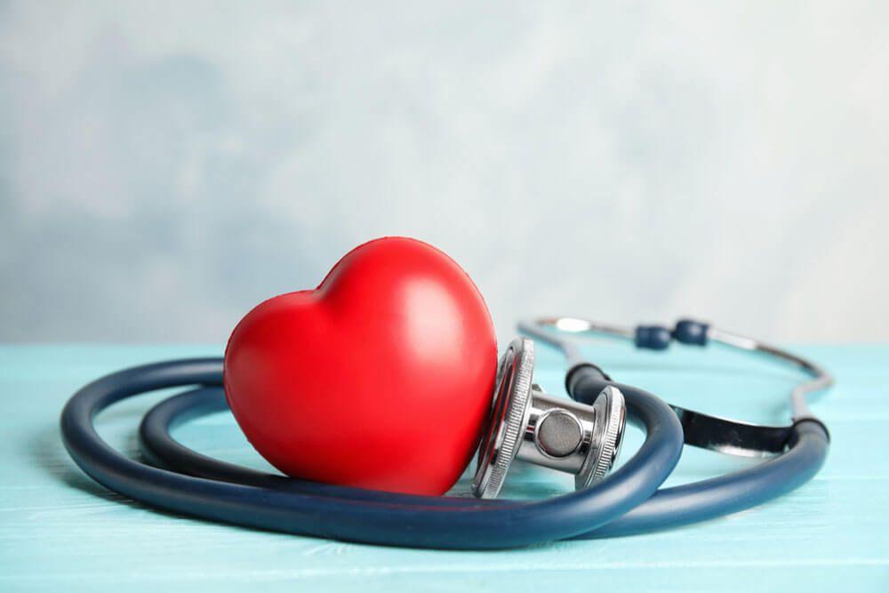 Stethoscope and red heart on wooden table.