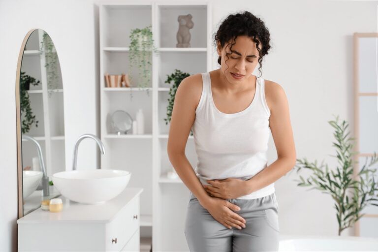 Young African-American woman suffering from menstrual cramps in bathroom