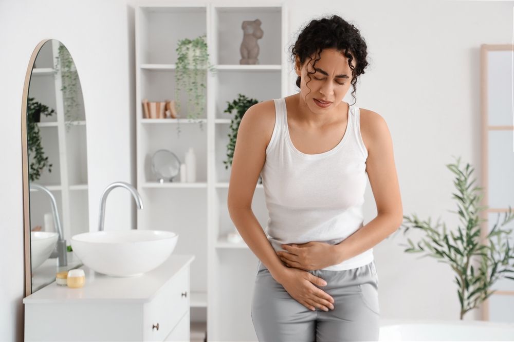 Young African-American woman suffering from menstrual cramps in bathroom
