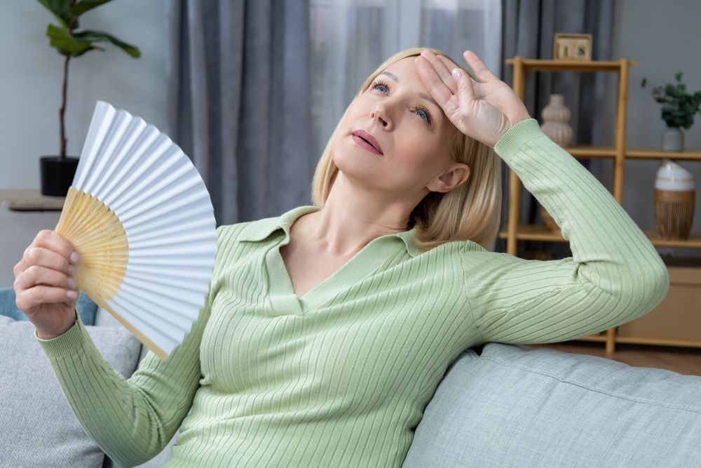 50 year old woman sitting with a fan in hand and suffering from heat