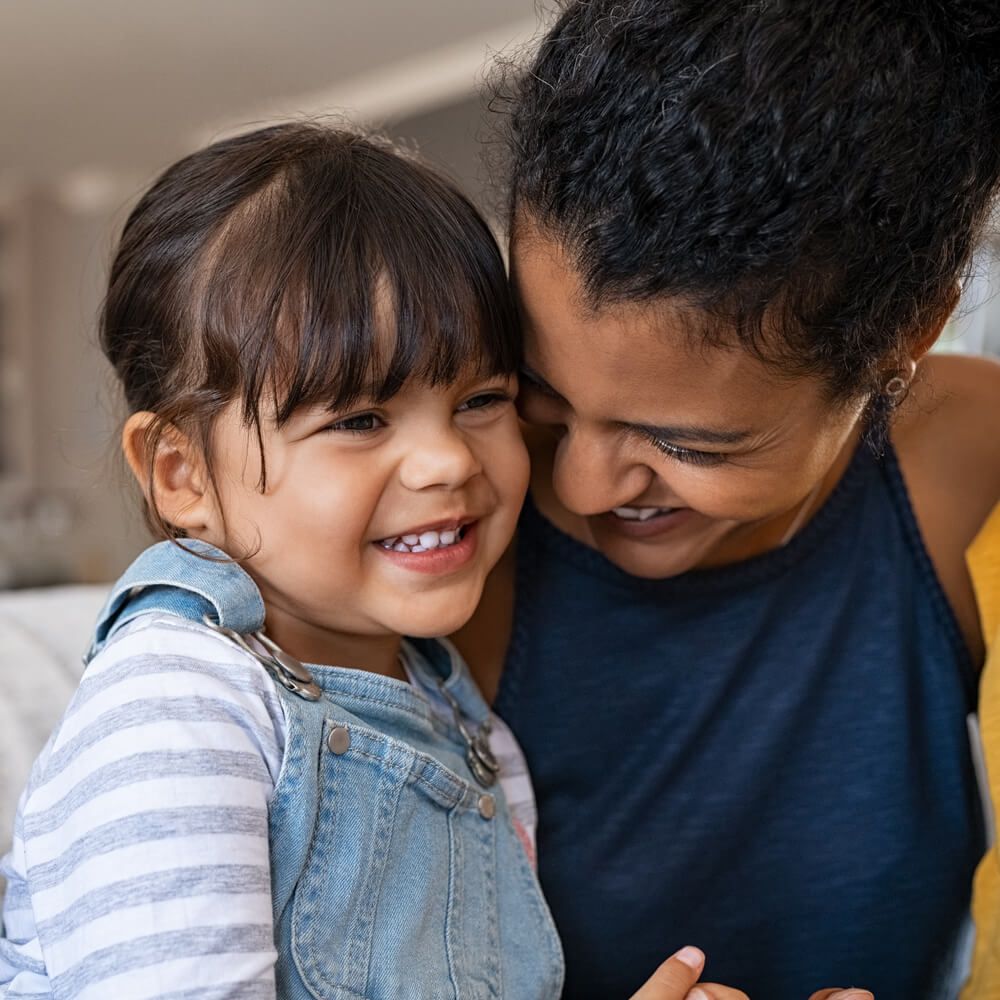 Beautiful black mother embracing little girl sitting on couch