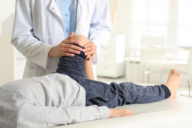 Professional orthopedist examining little patient's leg in clinic