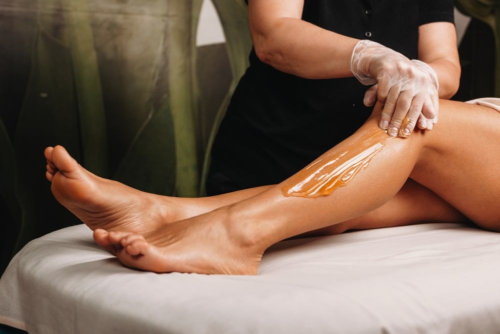 Caucasian spa professional having a sugaring session on legs for a charming woman