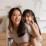 Happy asian mom holding her daughter playing together at home